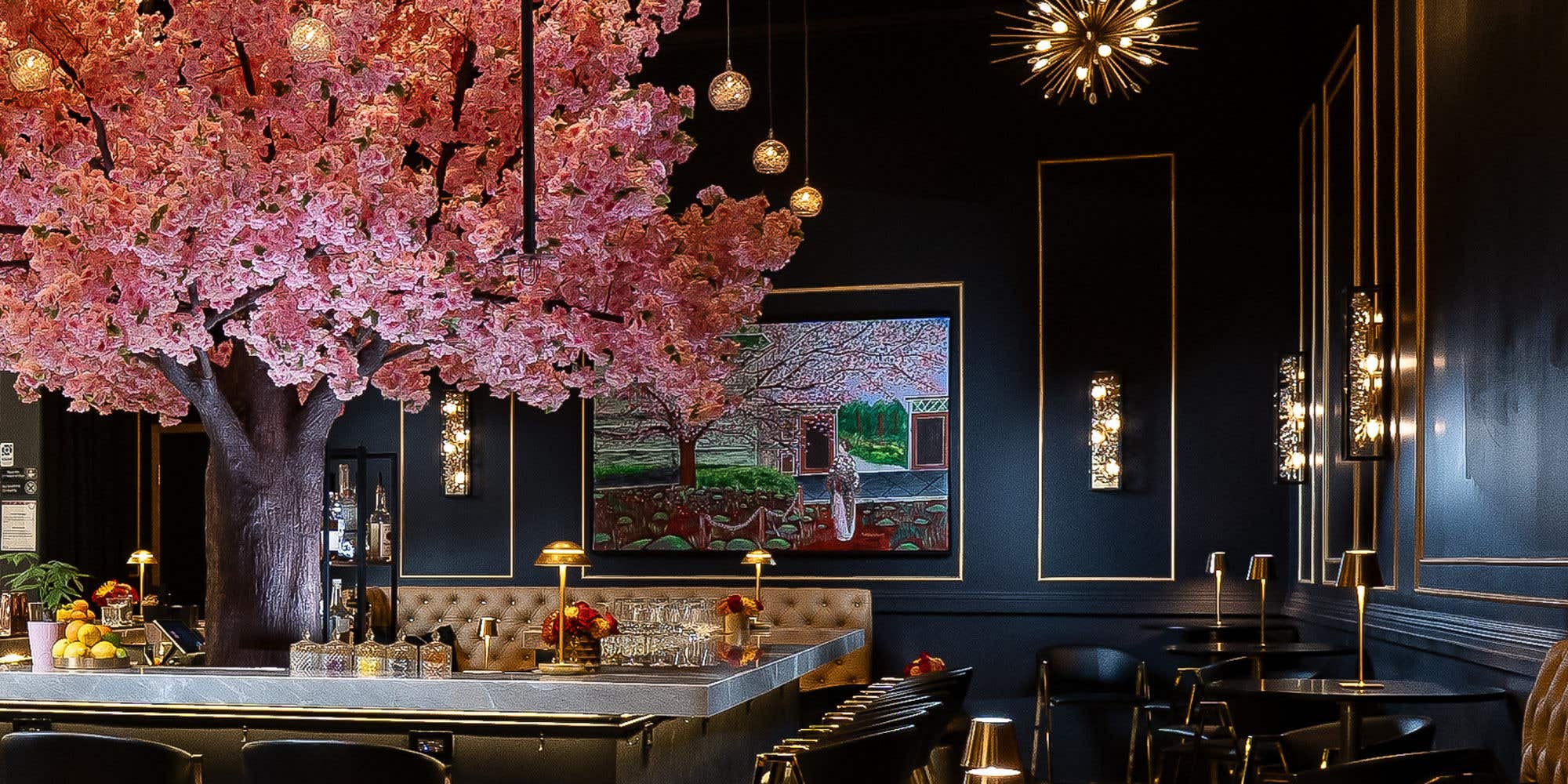 A bar with black walls, gold accents and a pink tree at the center.